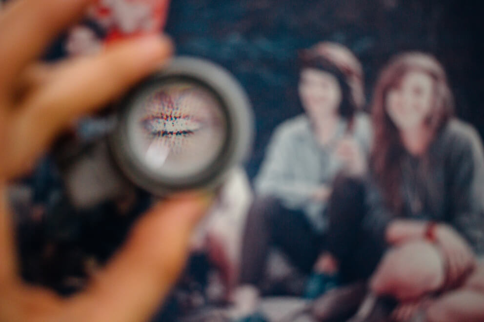 A hand holding a magnifiying loupe over a printed image. The focus of the photograph is set so that most of the image is blurry, except for printed dots in the magnifying glass